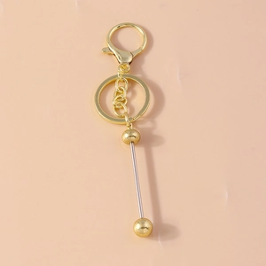 Golden geometric bead keychain accessory with metallic barbell charm on pink background