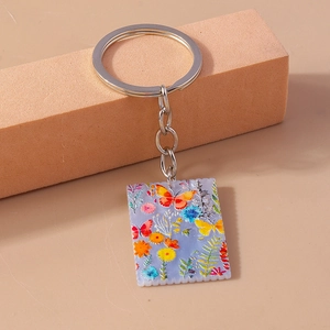 Detail view of square acrylic butterfly keychain with floral painting on a display stand