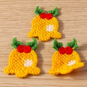 Close-up of yellow crochet Christmas bells with red roses and white snowflakes on wood