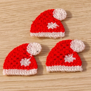 Close-up of three handmade crochet mini Christmas hats with white pom-poms on wood surface