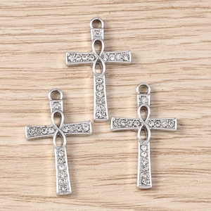 Macro detail of three silver infinity cross pendants with clear crystals on wood