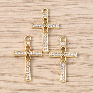 Close-up of golden infinity cross charms with pave rhinestones on a wood background