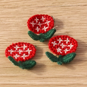 Close-up of handmade red crochet flower accessories with green leaves on wood