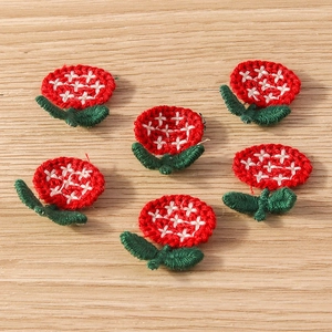 Detail of six small red embroidered flower patches with green leaves on wooden background
