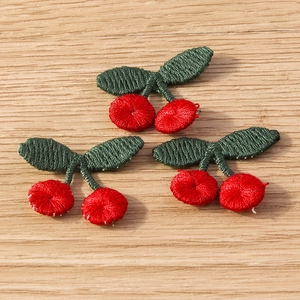 Detail of red cherry embroidery patches with green leaves on light wood background
