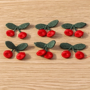 Detail of 6 handmade knit cherry charms with red balls and green leaves on wood