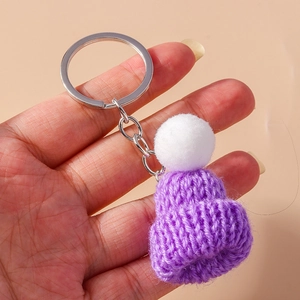 Close-up of a handmade purple knitted hat keychain with a white pompom held in hand