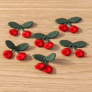 Detail showing red cherry embroidered patches on light wood background for DIY crafts