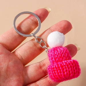 Close-up of a handmade mini rose pink knitted hat keychain with a soft white pompom detail