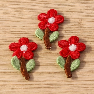 Close-up of three red flower embroidery patches with green leaves on wood surface