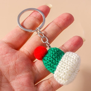 Mini hand-knitted hat keychain with red pom-pom and green-white stripes held in hand
