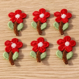 Close-up of red flower embroidery patches with green leaves on a wood background