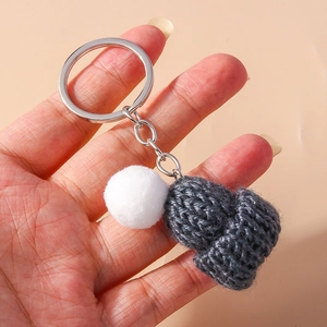 Close-up of a dark grey knitted mini hat keychain with white fluffy pom-pom and silver ring