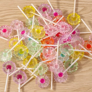 Colorful resin daisy lollipop charms with metal loops scattered on a wooden background