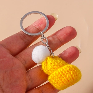 Handheld view of bright yellow knitted mini hat keychain with a white fluffy pompom