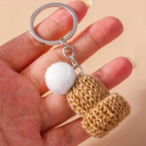 Detailed view of handmade knitted mini beanie keychain with white pompom held in hand