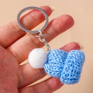 Detail of sky blue knitted hat keychain with white pompom held in hand with silver ring