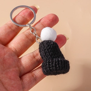 Close-up of handmade mini knit beanie keychain with black yarn and white fluffy pom-pom