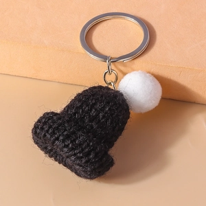 Detail view of mini knitted hat keychain with black yarn and white fuzzy pompom accessory