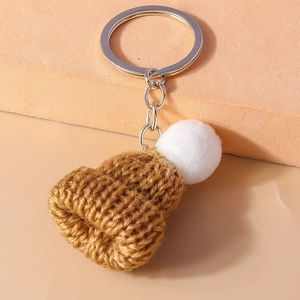 Detail of a brown knitted mini hat keychain with a white pompom and silver metal ring