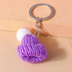 Detailed view of handmade purple knitted hat keychain with a soft white pompom detail
