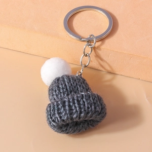 Detail of grey knitted hat keychain with white pompom on warm orange background