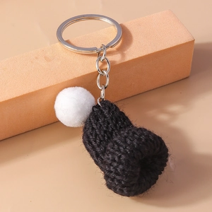 Detail of a handmade black knitted mini hat keychain with a white pompom and silver ring