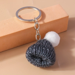 Close-up of handmade dark grey knit hat keychain with white pompom and metal ring