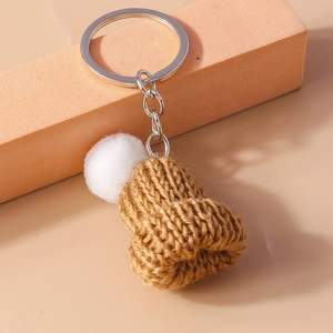 Close-up of caramel knitted mini hat keychain with white fluffy pompom and silver ring