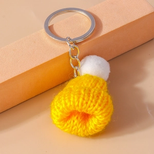 Macro detail of yellow knitted mini hat keychain with fluffy white pom-pom and metal ring