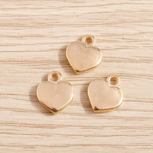 Three gold heart alloy pendants with top loops on a light wood background for DIY jewelry
