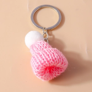 Pink knitted beanie keychain with a white pompom and silver ring on orange background