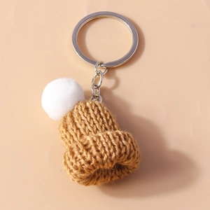 Detailed shot of handmade knit beanie keychain in caramel brown with a white pom pom