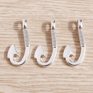 Macro detail of three silver fish hook pendants with textured design and metallic luster