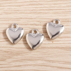 Close-up of three 3D silver heart pendants with smooth metallic finish on wood background