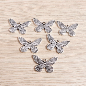 Vintage silver butterfly alloy pendants with detailed textures on wooden background