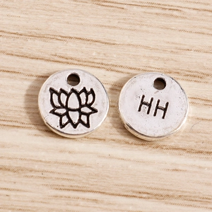 Macro detail of silver lotus and HH engraved round metal charms for DIY jewelry making
