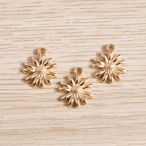 Vue macro de trois pendentifs marguerites en alliage doré sur fond de bois clair