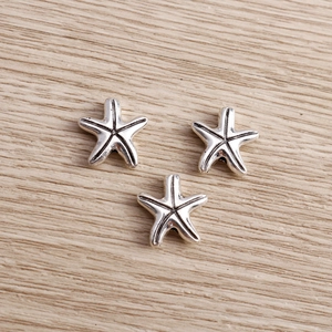 Antique silver starfish alloy charms for DIY jewelry making sets on wooden background