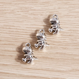 Three antique silver dinosaur charms for DIY jewelry making on a light wooden background