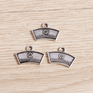 Detailed view of vintage silver nurse hat pendants with a classic cross symbol for DIY crafts