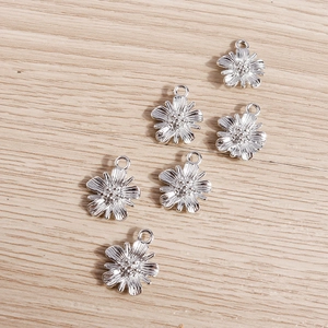 Close-up of six silver daisy flower pendants with hanging loops on wood background