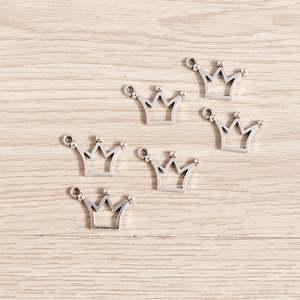Detail of silver alloy hollow crown pendants with matte texture on wooden background