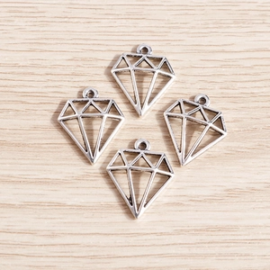 Détail de quatre pendentifs losanges creux en alliage d'argent rétro sur fond de bois clair