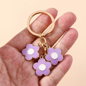 Detailed view of purple cherry blossom keychain charms with gold metal rings and oil drip finish