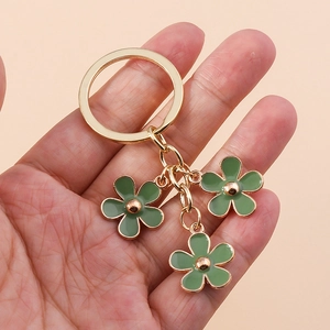 Golden cherry blossom keychain with green enamel flower pendants held by hand