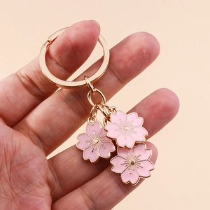 Porte-clés fleurs de cerisier roses avec anneau doré en métal tenu à la main