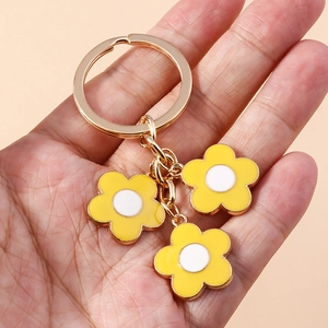 Detail shot of three yellow daisy charms with white enamel centers on a gold keychain