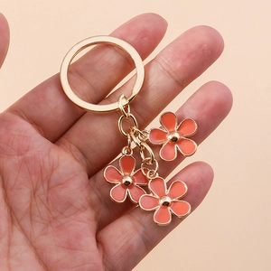 Close-up of golden keychain with three orange cherry blossom enamel flower pendants