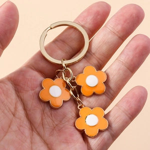 Detail of gold metal keychain with three orange and white enamel flower pendants in hand